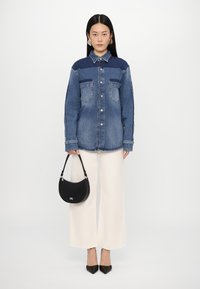 Camicia di jeans nei toni di blu chiaro e scuro, dotata di due tasche sul petto e chiusura con bottoni. Abbinata a pantaloni a gamba larga di un bianco sporco e a una borsa nera.