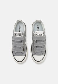 Hallid hallid kanvasportsid elastsete rihmadega, valge kummist varbakattega ja mustade aktsentidega. Omab "Converse All Star" silti keelel.