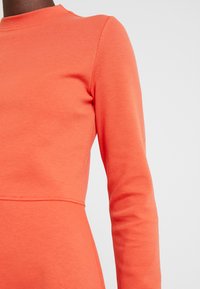 Långärmad topp i klar korall, tillverkad av slätt tyg med rundad halsringning och sömdetaljer vid midjan.