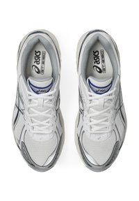 White athletic sneakers with mesh upper and plastic accents, featuring grey detailing, rounded toe, and flat laces. Logo on tongue and insole.