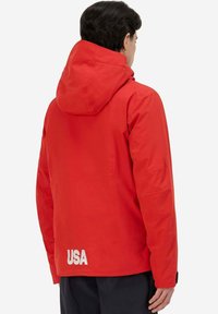 Giacca impermeabile rossa con cappuccio, caratterizzata da un logo "USA" bianco sul retro, realizzata in materiale liscio e con un design aderente.