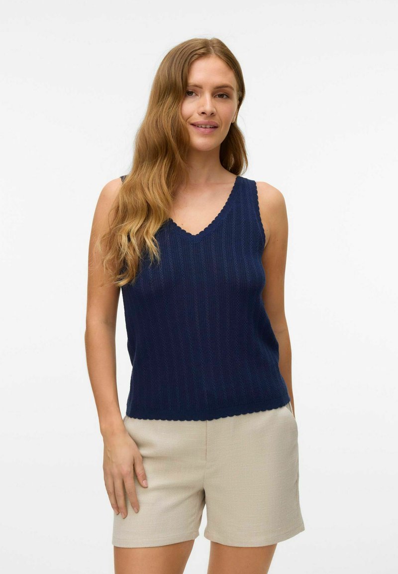 Top da tank in maglia a coste di colore blu navy, con scollatura a V bordata e spalline larghe, abbinato a pantaloni corti testurizzati di colore beige chiaro.