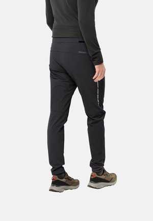 Pantalon de sport noir à coupe fuselée avec une ceinture texturée. Présente des accents réfléchissants gris le long du côté. Porté avec des baskets marron.