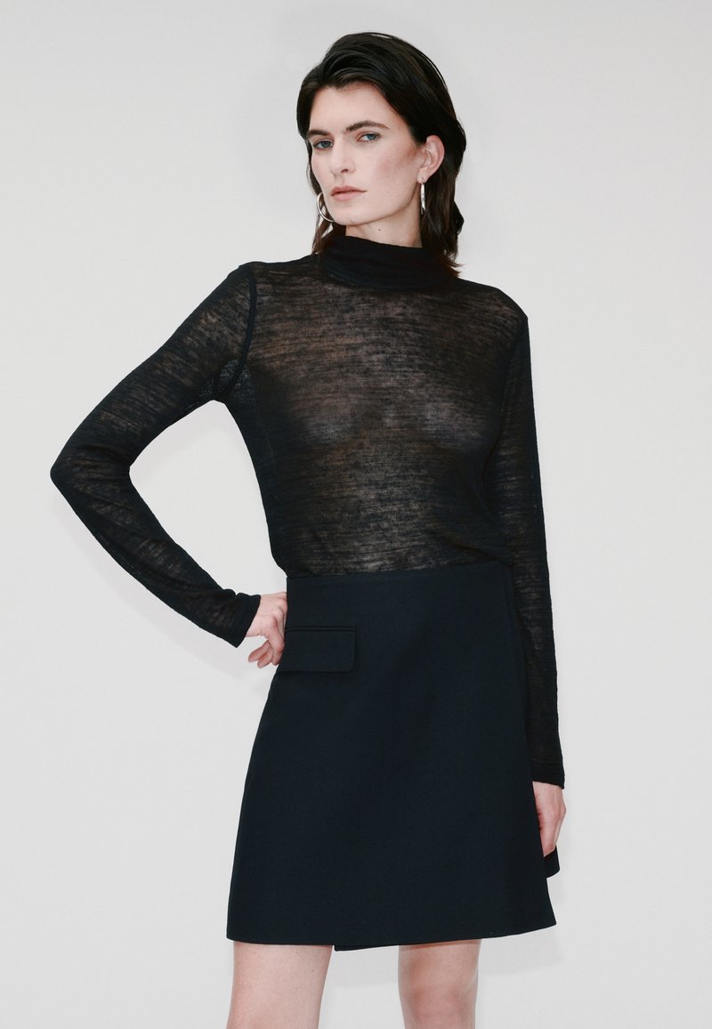 Haut transparent noir à manches longues avec un col montant, associé à une jupe évasée noire avec une poche latérale et une texture lisse.