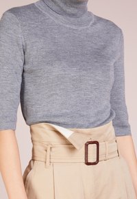 Suéter de cuello alto gris con mangas cortas, combinado con pantalones de cintura alta beige que cuentan con un cinturón ancho y una hebilla rectangular marrón.