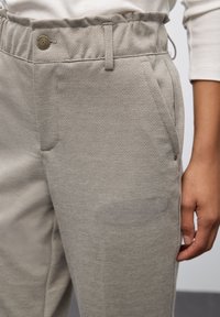 Ljusgrå, strukturerade byxor har en elastisk midja, sidofickor och en knappdetalj vid midjan för säker stängning.
