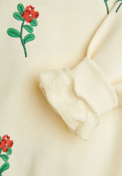 Tessuto a maglia cremoso con ricami floreali rossi e foglie verdi. La manica presenta un polsino testurizzato e arricciato di un colore crema più chiaro.