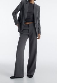 Grau maßgeschneiderter Anzug mit einem taillierten Blazer mit Reverskragen und weit geschnittenen Hosen. Glatte Stoffqualität, minimalistisches Design.