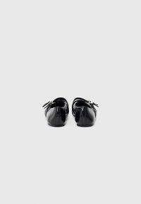 Black ballet flats with a glossy finish, round toe, and decorative bow on the back. Soft leather material with a low, flexible heel.