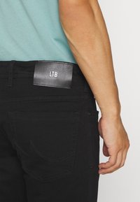 Svarta denimjeans med en läderetikett från LTB på baksidan. Har sydda fickor och en slim fit-design. Baksidan visar minimal detaljer.