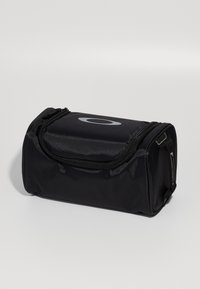 Borsa nera compatta con zip realizzata in tessuto resistente, con un logo grigio prominente, forma arrotondata e superficie testurizzata per una migliore presa.
