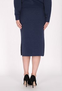 Gebreide lange marineblauwe rok met een ribbelrand, voorzien van zijsplitten en gecombineerd met zwarte hoge hakken. Textuur van de stof is afgewerkt.
