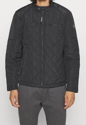 Hombre con chaqueta acolchada negra con cremallera frontal, bolsillos en el pecho y laterales con cremallera, y cierre de cuello con botón de presión.