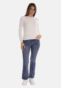 Top bianco a maniche lunghe con scollo rotondo, abbinato a jeans a campana blu e sneakers bianche. Tessuto liscio con una vestibilità aderente.