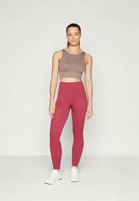 Top cropped castanho e leggings altas rosa escuro. As leggings têm uma textura suave, combinadas com sapatilhas brancas.