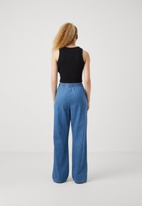 Black sleeveless top paired with light blue, loosely fitting denim pants that have an elastic waistband and a straight-leg design.