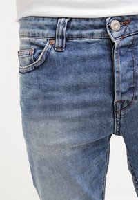 Blue denim jeans feature a fitted design, five-pocket styling, copper rivets, and light fading for a worn look. Textured fabric visible.