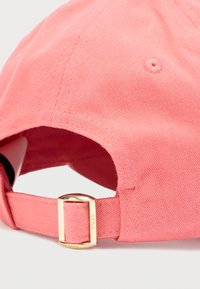 Koralowa bawełniana czapka bejsbolowa z miękką, teksturowaną powierzchnią i metalową sprzączką z tyłu. Posiada przeszyty wierzch i markowy detal.