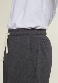 Gray sweatpants with an elastic waistband, white drawstring, side pockets, and visible stitching details. Fabric appears soft and textured.