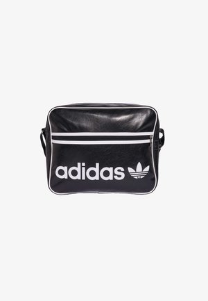 Sac à bandoulière noir Adidas avec passepoils blancs, poche avant zippée, et grand logo Adidas blanc avec trèfle à l’avant.