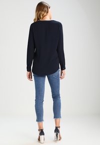 Marinblus med lång ärm och rundad nederkant, kombinerad med ljusblå skinny jeans. Outfiten har silverfärgade klackskor med blockklack.