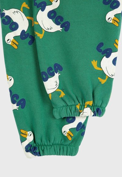 Green cotton pants featuring a repeated goose pattern with blue text "LA OCA." Elastic cuffs at the ankles for a fitted look.