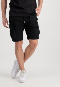 Pantalones cortos de carga negros hechos de algodón con un corte holgado. Presentan múltiples bolsillos y una cintura con cordón. Combinados con zapatillas blancas.