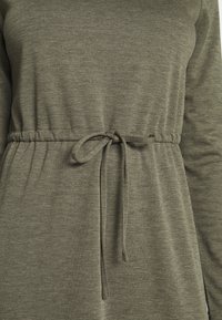 Oliwkowa sukienka z teksturowanym wykończeniem, posiadająca elastyczny pas i długie rękawy. Gładki materiał o casualowym kroju.