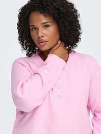 Pink knitted sweater with a V-neck, featuring three heart-shaped buttons. The fabric appears soft and textured, with long sleeves.