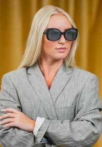 Grå stribet blazer med en afslappet pasform, parret med store sorte solbriller. Langt blondt hår og en hvid knappet skjorte er synligt.
