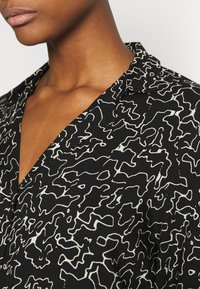 Blusa nera con un motivo bianco fluido e ondulato. Presenta un colletto a V e una texture morbida, che mette in risalto il design intorno al collo.