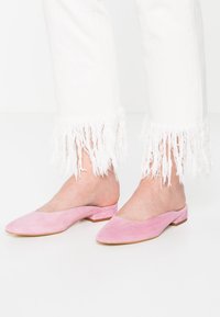 Růžové semišové muly s nízkým blokovým podpatkem, s špičatou špičkou a elegantním designem, spárované s bílými džíny s třásněmi na lemech.