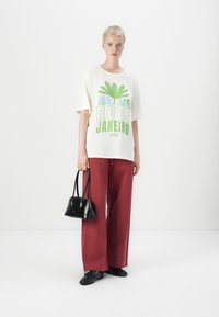 T-shirt en coton blanc avec un graphique vert et violet "RIO DE JANEIRO 1995", assortie à un pantalon rouge ample et un petit sac à main noir.