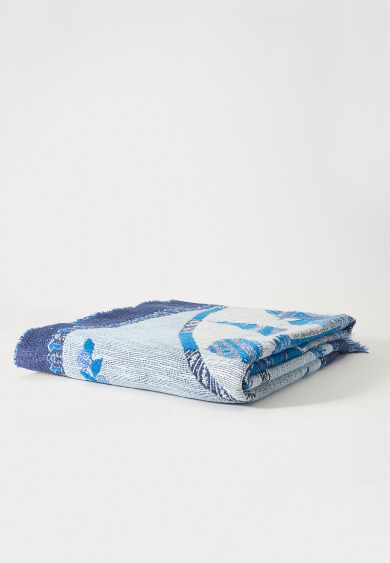 Serviette en coton pliée avec des motifs bleus et blancs posée sur une surface blanche.