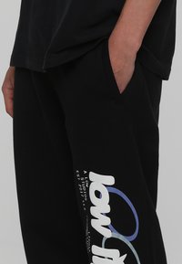 Svarta joggingsbyxor i bomullsblandning, med sidofickor och en vit design med färgade accenter på vänster ben.