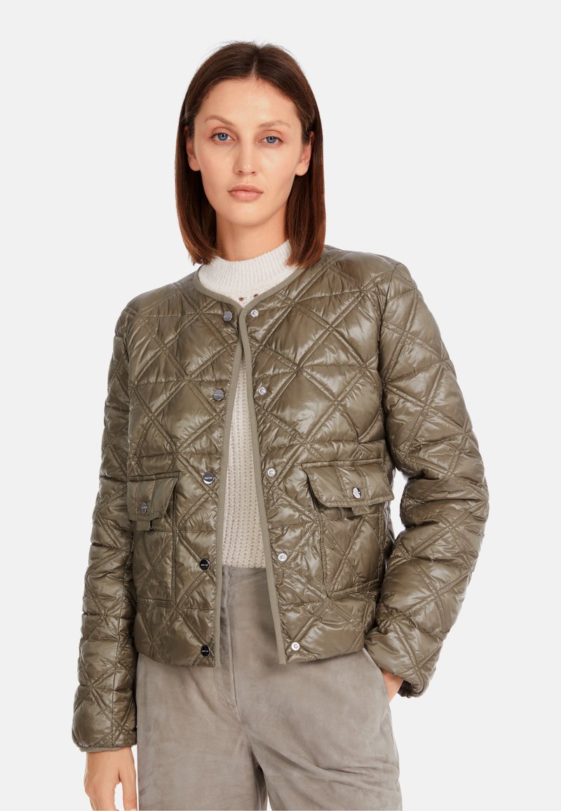 Quilted olivgrüne Jacke mit Rundhalsausschnitt, Druckknopfverschlüssen und zwei vorderen Taschen. Strukturiertes, glänzendes Finish und darunter ein gerippter Pullover.