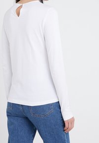 Maglietta bianca a maniche lunghe realizzata in tessuto morbido, con dettaglio a chiave sulla schiena, abbinata a jeans in denim.