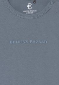T-shirt de algodão azul com decote redondo, apresentando o texto "BRUUNS BAZAAR" em azul claro, tamanhos indicados na etiqueta. Textura suave e lisa.