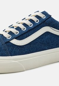Zapatillas de lona en azul oscuro con suela de goma blanca, detalle de cordones y un distintivo diseño de franja lateral blanca. Acabado de tela texturizada.