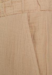 Tissu en lin beige avec une finition texturée légèrement froissée. Présente une couture visible et un grain à motif subtil sur toute la surface.