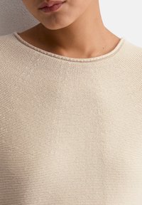 Hellbeige Strickpullover mit rundem Ausschnitt, strukturiertem Stoff und dezenten Rippelementen entlang des Kragens.