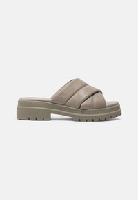 Sandale beige à enfiler avec brides croisées rembourrées, semelle épaisse et robuste, et logo en creux d'arbre sur le côté.
