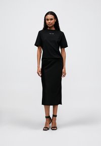 Black t-shirt with short sleeves, featuring a small graphic on the chest, paired with a black satin midi skirt and black strappy heels.