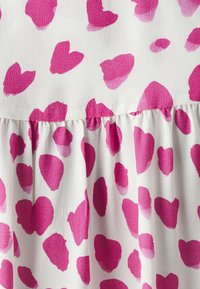 Tessuto bianco con macchie a forma di cuore rosa, caratterizzato da una superficie testurizzata e un dettaglio arricciato lungo il fondo. Motivo vivace e giocoso.