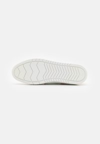Semelle de chaussure en caoutchouc blanc avec un motif de crampons en zigzag, présentant des textures géométriques surélevées pour l'adhérence et la stabilité.