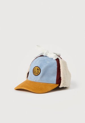 Gorra azul de pana con visera color mostaza, paneles laterales burdeos, orejeras de forro polar color crema y un lazo blanco en la parte superior.