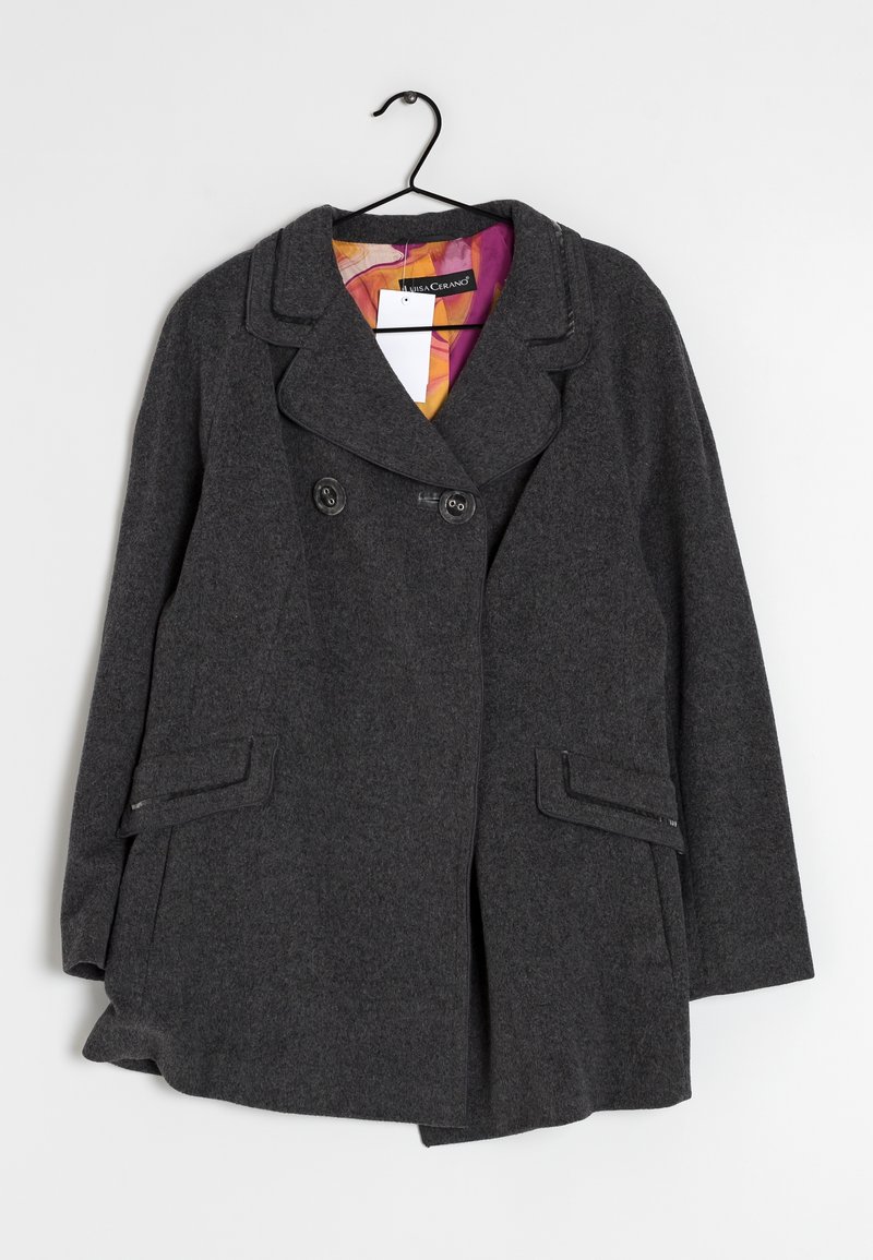 Cappotto di lana grigio con bottoni doppi, ampio colletto, tasche laterali e una fodera interna con un motivo colorato. Appeso a un gancio.