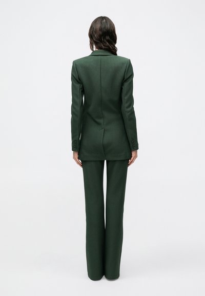 Tmavozelený oblek na mieru s priliehavým sako a nohavicami so širokými nohavicami. Hladká tkanina, štruktúrované ramená a zapínanie saka na jeden gombík.