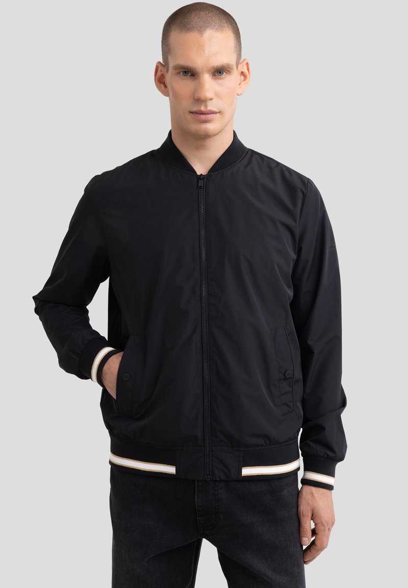 Juodas bomberio tipo švarkas su raukinėtu apykakle ir rankogaliais, su užtrauktuku ir šoniniais kišeniais, pagamintas iš lygaus, lengvo audinio.