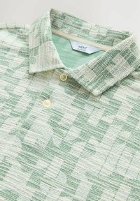 Chemise texturée verte et blanche à manches courtes avec un motif à carreaux, col boutonné et étiquette « NEXT Relaxed Fit » à l'intérieur de l'encolure.